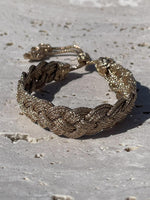 Bracelet en passementerie tressée couleur or antique, technique Sfifa, 100% fil à effet or, fait main au Maroc, cordons coulissants à embouts décoratifs, posé sur pierre claire.