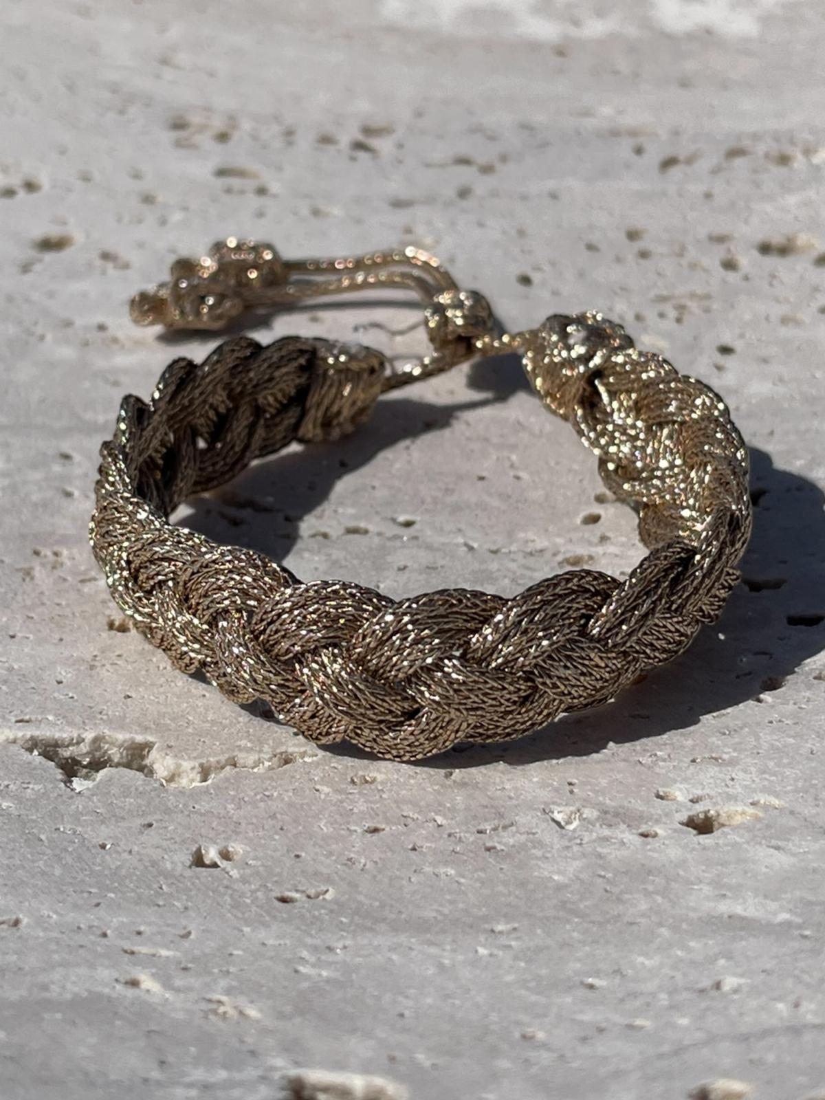 Bracelet en passementerie tressée couleur or antique, technique Sfifa, 100% fil à effet or, fait main au Maroc, cordons coulissants à embouts décoratifs, posé sur pierre claire.