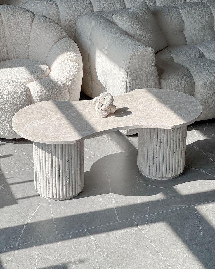 Table basse en travertin naturel aux pieds cylindriques striés, mise en scène dans un salon bohème chic avec canapé beige, tapis crème et plante verte.